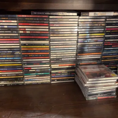 Sale Photo Thumbnail #164: Large collection of compact discs and DVDs stacked in jewel cases, featuring various R&B, hip-hop, and pop titles from the 1990s and 2000s.