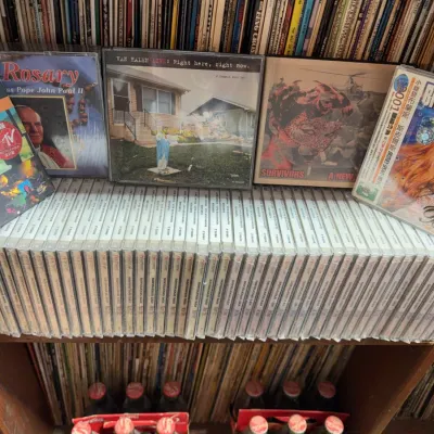 Sale Photo Thumbnail #140: Large collection of compact discs, including pop, rock, and spoken word titles alongside a row of jewel cases.