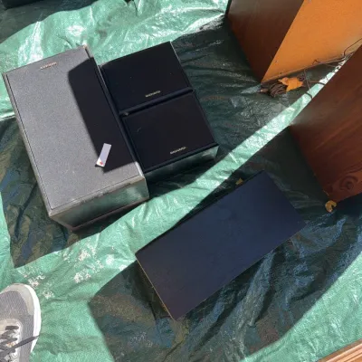 Sale Photo Thumbnail #58: Selection of vintage Magnavox audio speakers in black cabinets with cloth grilles resting on a green tarp.