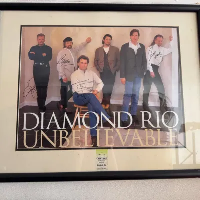 Sale Photo Thumbnail #135: Framed and matted autographed promotional poster for Diamond Rio's album 'Unbelievable', featuring signatures from band members.