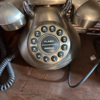 Sale Photo Thumbnail #163: Vintage-style brushed metallic telephone with a push-button rotary-look dial pad, featuring flash and redial options.