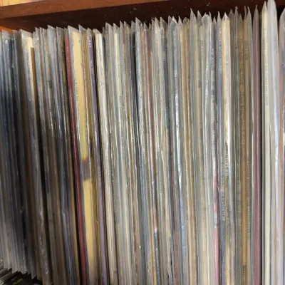 Sale Photo Thumbnail #110: Large collection of vintage vinyl LP records, individually stored in protective plastic sleeves on a wooden shelf.