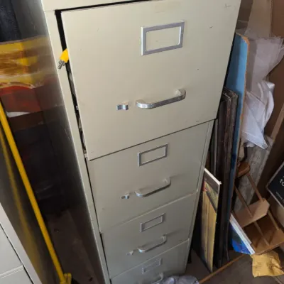 Sale Photo Thumbnail #186: Tall beige metal four-drawer vertical filing cabinet, featuring silver-tone handles and label holders, showing moderate wear and minor surface marks.
