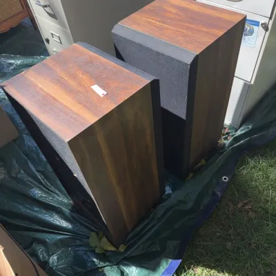 Sale Photo Thumbnail #51: Pair of vintage stereo floor speakers with wood grain cabinets and black fabric grilles, shown outdoors on a tarp.