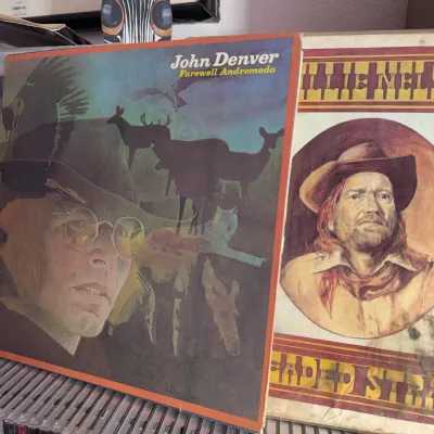 Sale Photo Thumbnail #132: Vintage vinyl LP records including John Denver's 'Farewell Andromeda' (1973) and Willie Nelson's 'Red Headed Stranger' (1975) displayed above a row of CDs.