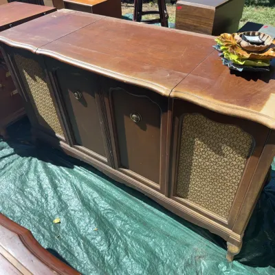 Sale Photo Thumbnail #63: Vintage mid-century wooden stereo console with patterned fabric speaker grilles and brass hardware, showing some surface wear.