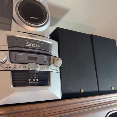 Sale Photo Thumbnail #149: Audiovox silver shelf stereo system featuring a 5-CD changer, cassette deck, matching speaker, and a pair of black cloth-grille bookshelf speakers.