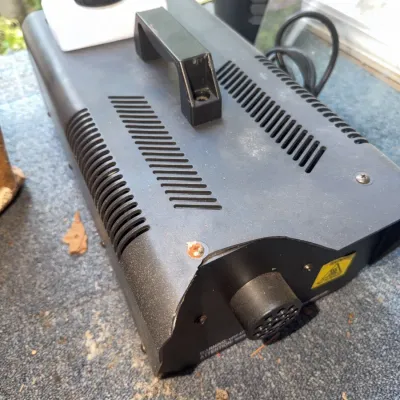 Sale Photo Thumbnail #173: Portable black metal fog machine featuring a fluid reservoir, carrying handle, and output nozzle. Shows minor surface wear and corrosion near a top screw.