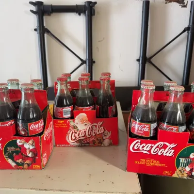 Sale Photo Thumbnail #142: Three vintage six-packs of Coca-Cola Classic glass bottles with Santa Claus holiday packaging, dated 1996, 1997, and 1999.
