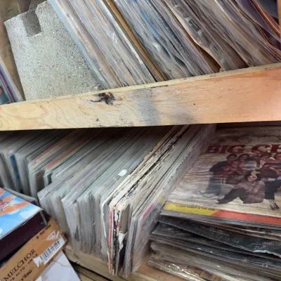 Sale Photo Thumbnail #93: Large collection of vintage 45 RPM vinyl records in sleeves, stacked on wooden shelving.