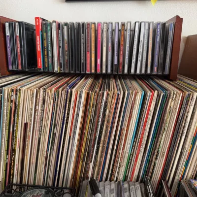 Sale Photo Thumbnail #136: Large collection of vintage vinyl LP records alongside a wooden rack filled with CD-ROM software and computer games, primarily from the 1990s.