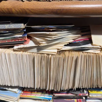 Sale Photo Thumbnail #108: Large collection of vintage 45 RPM vinyl records in paper sleeves stacked on shelves.