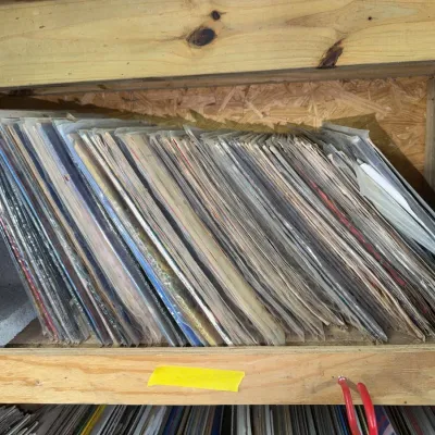 Sale Photo Thumbnail #90: Large collection of vintage vinyl LP records stacked on a wooden shelf, many in protective plastic sleeves.
