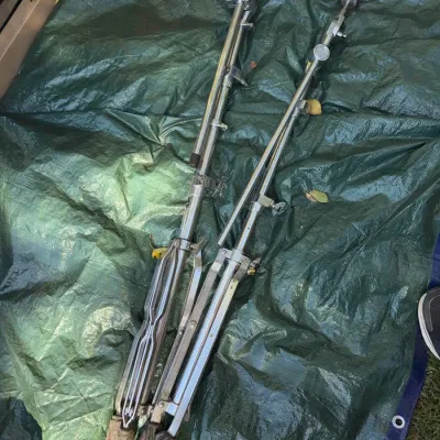 Sale Photo Thumbnail #46: Pair of collapsible chrome drum cymbal stands, including one boom arm stand, resting on a green tarp.