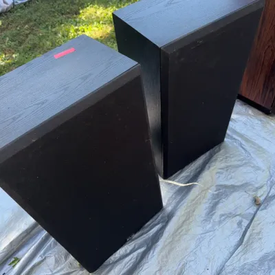 Sale Photo Thumbnail #38: Pair of black woodgrain KLH bookshelf speakers with fabric grilles, resting outdoors on a tarp.