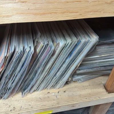 Sale Photo Thumbnail #86: Collection of vinyl records stored in protective plastic sleeves on a wooden shelf.