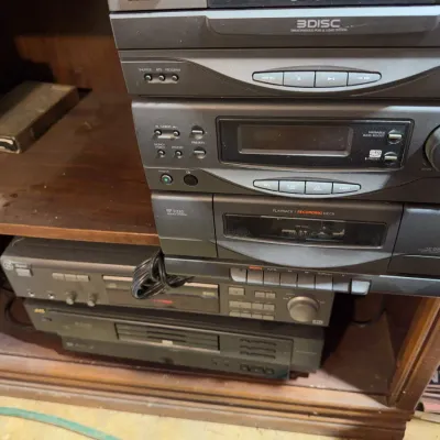 Sale Photo Thumbnail #171: Stack of vintage black stereo audio components, including a 3-disc CD changer, cassette deck, and tuner, resting inside a wooden cabinet.