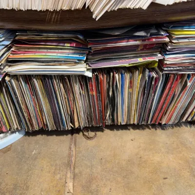 Sale Photo Thumbnail #109: Large collection of vintage vinyl records in paper sleeves, stacked horizontally and vertically on low wooden shelving.