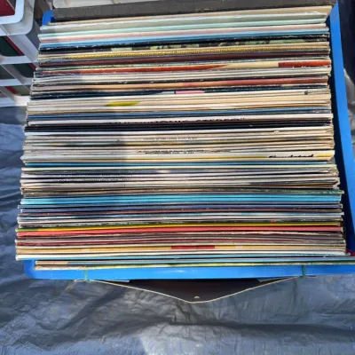 Sale Photo Thumbnail #30: Large stack of vintage vinyl LP records in cardboard sleeves stored inside a blue plastic crate.
