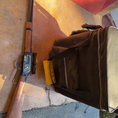 Sale Photo Thumbnail #95: Daisy Grizzly lever-action BB gun with mounted scope alongside an olive green soft-sided canvas cooler bag.