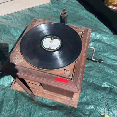 Sale Photo Thumbnail #65: Vintage hand-crank tabletop phonograph in a wooden cabinet, featuring a vinyl record on the turntable.