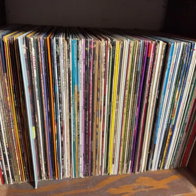 Sale Photo Thumbnail #126: Large collection of vintage vinyl LP records stacked vertically on a wooden shelf.