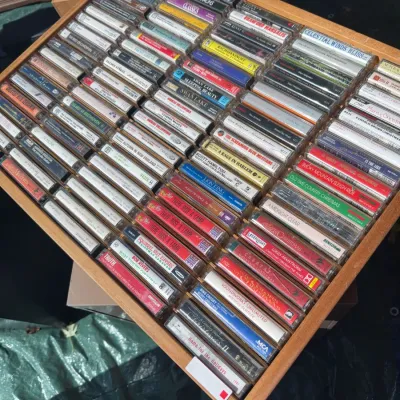 Sale Photo Thumbnail #54: Large wooden storage tray filled with vintage cassette tapes featuring various musical artists and genres.