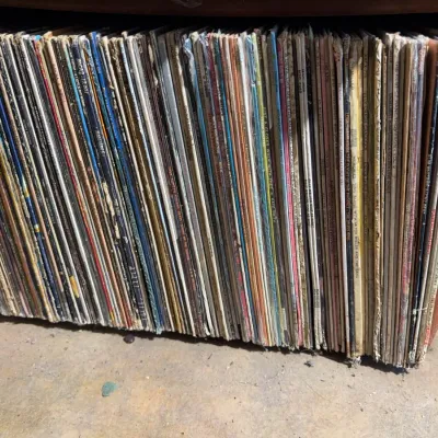 Sale Photo Thumbnail #114: Large collection of vintage 33 RPM vinyl records stored vertically in a wooden shelf unit.