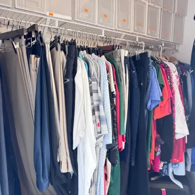 Sale Photo Thumbnail #150: Closet filled with assorted modern men's and women's clothing, clear plastic shoe storage boxes on wire shelving, and luggage below.