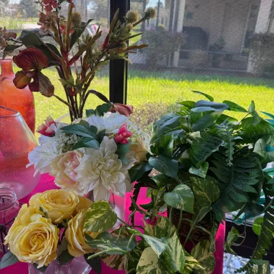 Collection of faux floral arrangements and artificial potted green plants, including silk yellow roses and tropical foliage displayed in...