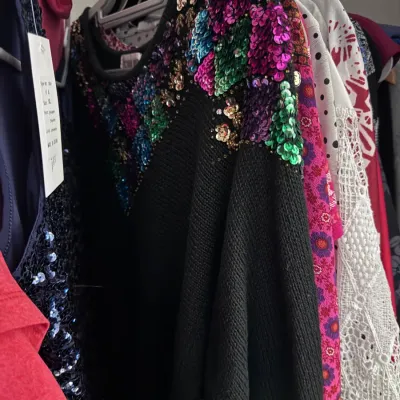 Sale Photo Thumbnail #152: Vintage 1980s black knit sweater embellished with colorful sequined floral patterns along the shoulders and neckline, hanging among other garments.