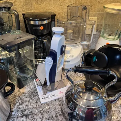 Sale Photo Thumbnail #130: Collection of small kitchen appliances including blenders, a Black & Decker drip coffee maker, Cuisinart food processor, slow cooker, stainless steel tea kettle, and a SafeSlice mandoline slicer.