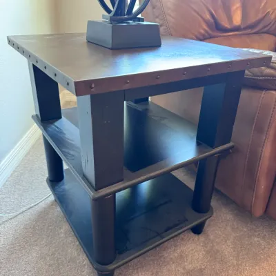 Industrial-style wooden side table featuring a metal tabletop with nailhead trim and two lower display shelves.