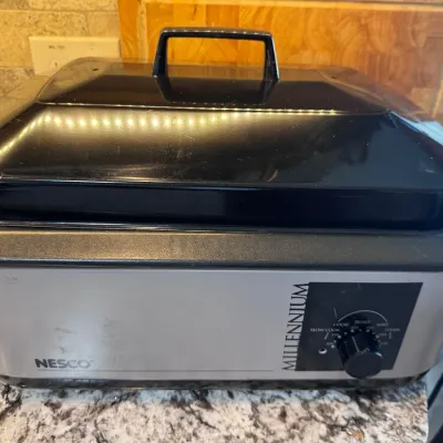 Sale Photo Thumbnail #132: Nesco Millennium electric roaster oven with a black lid and temperature control dial.