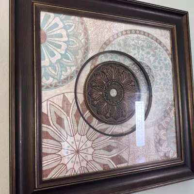 Sale Photo Thumbnail #149: Framed mixed-media wall art featuring printed mandala patterns and a central raised bronze-tone medallion, encased in a dark wooden frame.