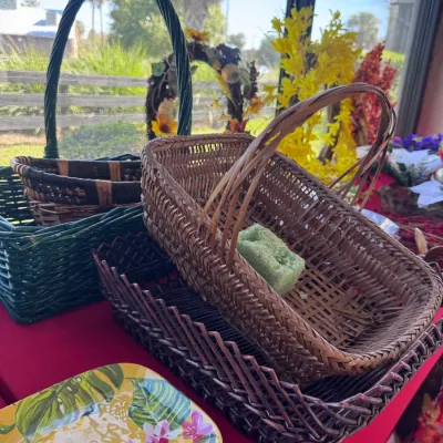 Assortment of woven wicker baskets with handles and a colorful botanical print serving tray displayed on a red tablecloth.