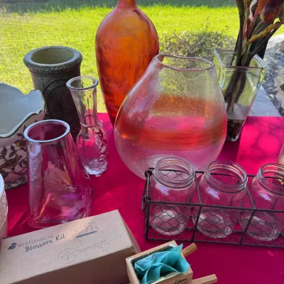 An assortment of decorative glass and ceramic vases, a wire caddy with three glass jars, and a wooden miniature wheelbarrow kit arranged...