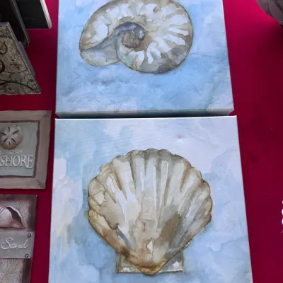 Pair of square wrapped canvas wall art prints featuring watercolor-style seashell designs on light blue backgrounds.