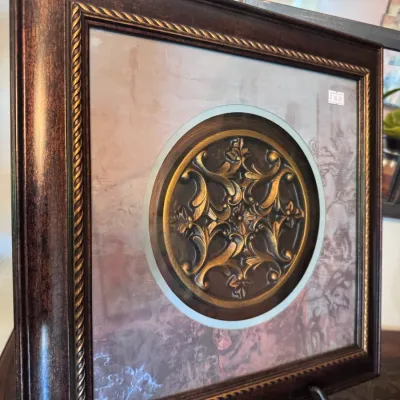 Framed traditional wall art featuring a relief-style ornate bronze medallion emblem set within a square textured background and...