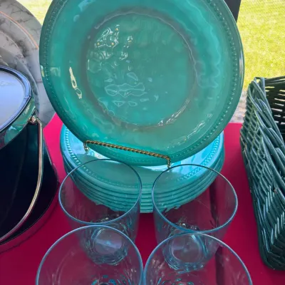 Set of turquoise beaded-rim melamine dinner plates paired with four matching tinted plastic tumblers, displayed alongside a dark green...