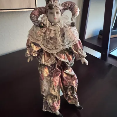 Vintage porcelain harlequin jester doll dressed in a metallic iridescent suit with a lace collar and jingle bells.