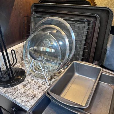 Sale Photo Thumbnail #128: Collection of bakeware including loaf pans, sheet pans, wire cooling racks, and glass pot lids stored on a wire rack.