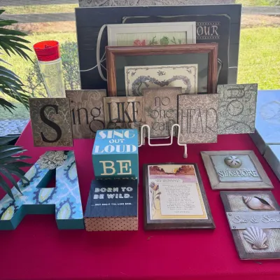 Collection of modern inspirational wall plaques, framed artwork, and decorative wooden blocks arranged on a red tablecloth.