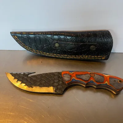 Sale Photo Thumbnail #98: Custom skinning knife featuring a gut hook blade with scale-textured spine, colorful Pakkawood handle, and a black faux-croc leather sheath.