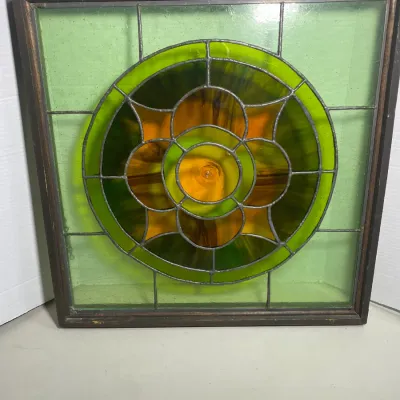 Sale Photo Thumbnail #119: Antique framed leaded stained glass window featuring a geometric circular design with green and amber glass panels.