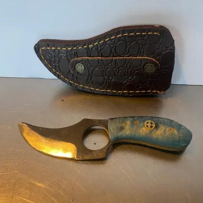 Sale Photo Thumbnail #97: Custom fixed-blade skinner knife with a finger hole, blue acrylic or stabilized wood handle scale with mosaic pin, alongside a matching alligator-embossed leather sheath with yellow stitching.