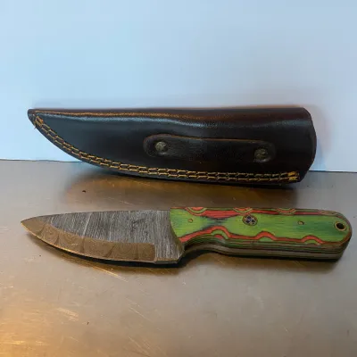 Sale Photo Thumbnail #68: Custom fixed-blade hunting knife with a Damascus steel blade and colorful layered Pakkawood handle, accompanied by a stitched brown leather sheath.