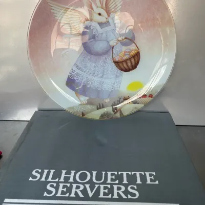 Sale Photo Thumbnail #44: Pilgrim Glass Silhouette Servers glass decorative plate featuring an illustration of an angelic rabbit carrying an Easter basket, presented with its original box.