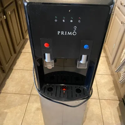 Sale Photo Thumbnail #117: Primo freestanding water dispenser with hot and cold temperature controls, featuring a stainless steel and black plastic casing.