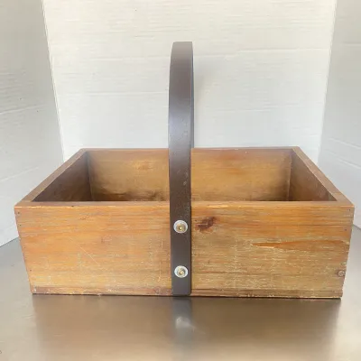 Sale Photo Thumbnail #26: Vintage rustic wooden tote basket with a dark metal handle, featuring a naturally weathered finish and bolted hardware.